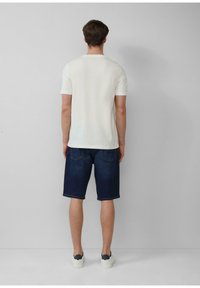 Wit T-shirt met korte mouwen, denim shorts in een donkere wassing, en witte sneakers. Eenvoudig ontwerp met een ronde halslijn en zichtbare achterzakken.