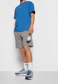 Blå bomullströja med en liten vit logotyp, grå shorts med en stor svart Nike-logotyp och blå sneakers med grå detaljer.