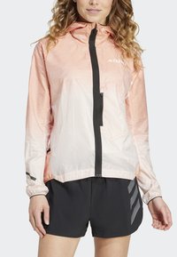 Veste légère à capuche dégradée de pêche à blanc avec une fermeture éclair et des accents noirs. Dispose d'une poche sur la poitrine et de poignets élastiques.