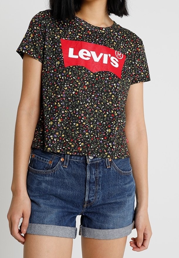 Camiseta negra de Levi's con estampado floral y mangas cortas, que presenta un gran logo rojo. Combinada con pantalones cortos de mezclilla azul con dobladillos doblados.