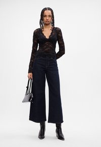 Zwarte kanten top met lange mouwen, een V-hals en geschulpte randen, gecombineerd met donkere wijde denim jeans en strakke zwarte enkellaarsjes met hak.