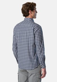 Camisa de cuadros azul y blanca de manga larga con puños abotonados y cuello puntiagudo, hecha de tela ligera, combinada con pantalones grises.
