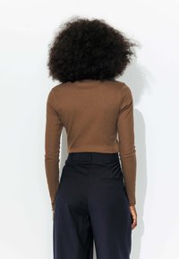 Haut marron à manches longues en maille côtelée associé à un pantalon à pinstripes navy taille haute. Le tissu semble doux avec une silhouette ajustée.