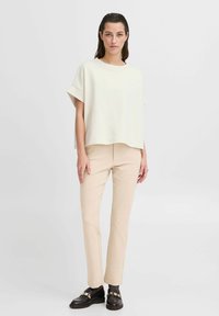 Ljusbeige oversized topp med korta ärmar, i kombination med åtsittande beige byxor och svarta skor med guldakenter.