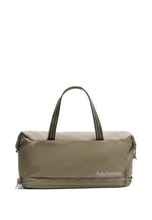 Bolsa de lona rectangular de color verde oliva con asas dobles y un compartimento con cremallera en la parte inferior, con la marca "lululemon" en blanco en la parte frontal inferior derecha.