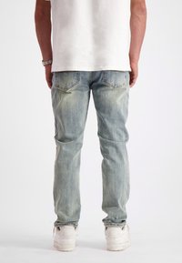 Lichtblauwe denim jeans met een rechte pasvorm, vervaagde afwerking en twee achterzakken, gedragen met witte sneakers en een effen wit shirt.