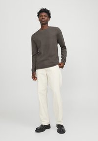 Camisa de manga larga texturada en gris oscuro combinada con pantalones de pierna ancha en color crema y zapatos gruesos negros, creando un atuendo casual.