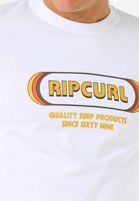 White t-shirt featuring a central logo with "RIP CURL" in bold black and yellow letters, and the text "QUALITY SURF PRODUCTS SINCE SIXTY NINE."