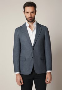 Męska marynarka szyta na miarę w ciemnoszarym kolorze, z wyłogami, dwoma przednimi kieszeniami, zapięciem na jeden guzik oraz gładką strukturą.