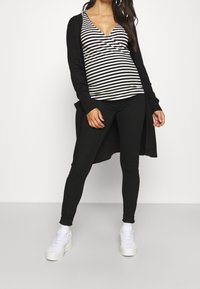 Black long cardigan over a black and white striped v-neck top, paired with black leggings and white sneakers, emphasizing a sleek, layered look.
