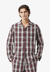 Kockás pizsama hosszú ujjakkal és gallérral, piros, zöld és kék vonalakkal fehér háttérrel. Tartalmaz egy mellzsebet logóval.