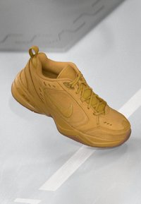 Geel Nike sneaker met zichtbare veters, swoosh-logo en gestructureerde zool op een grijze ondergrond met witte lijnen.