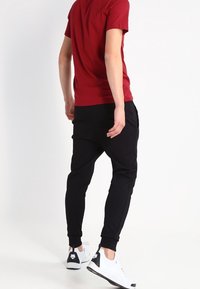 Czerwona koszulka z krótkim rękawem, czarne spodnie dresowe, białe sneakersy z czarnymi akcentami. Tkanina jest gładka; spodnie mają zwężany krój nogawek.