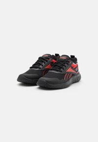 Chaussures de sport noires avec accents rouges, empeigne en maille, semelle texturée et logo. Comprend un système de laçage et un motif camouflage sur les côtés.