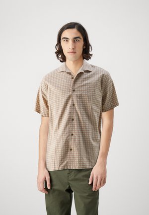 Camisa de manga corta, con botones, en un tejido color beige claro que presenta un patrón geométrico en marrón y crema. Diseño con cuello y un corte relajado.