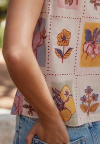 Short-sleeve, light fabric top featuring a patchwork floral pattern in yellow, pink, and blue with dotted accents. Casual fit with a rounded hem.