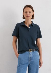 Marineblauwe katoenen polo met een kraag, korte mouwen en drie knopen. Gecombineerd met hoge lichtblauwe spijkerbroek.