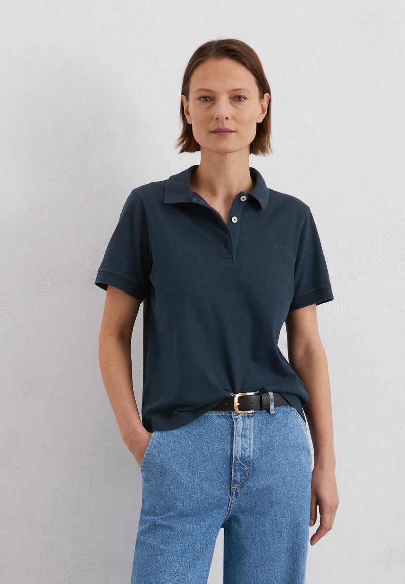 Marineblauwe katoenen polo met een kraag, korte mouwen en drie knopen. Gecombineerd met hoge lichtblauwe spijkerbroek.