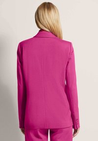Fuchsia blazer with structured shoulders, notch lapel, and long sleeves. Smooth fabric with two buttons at cuffs and central back seam.