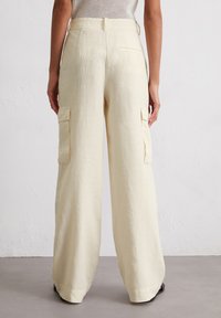 Helle gelbe Leinen-Cargohosen mit weitem Bein, ausgestattet mit zwei seitlichen Taschen und einer Gesäßtasche, vor einem neutralen Hintergrund.