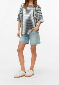 Randig, oversize grå och marinblå skjorta, kombinerad med ljusblå jeansshorts. Modellen bär vita sneakers med gummisulor.