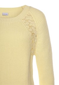 Żółty dziergany sweter z dekoltem w łódkę i koronkowymi panelami na ramionach, prezentujący teksturowany, prążkowany wzór.