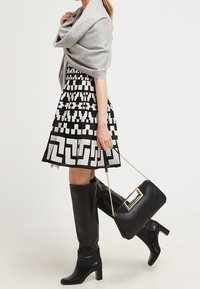 Vestido de estampado en blanco y negro con falda acampanada, chal gris, botas negras hasta la rodilla y un bolso negro con acento dorado.