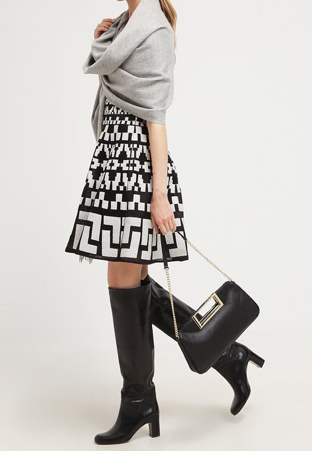 Vestido de estampado en blanco y negro con falda acampanada, chal gris, botas negras hasta la rodilla y un bolso negro con acento dorado.