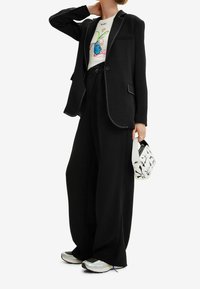 Czarna dopasowana marynarka z białym obszyciem, zestawiona z koszulką z grafiką, szerokimi czarnymi spodniami i białą torebką w wzory. Casualowe sneakersy.