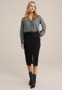 Bluză verde cu model, cu decolteu în V, închidere cu nasturi și mâneci lungi, asociată cu o fustă tip creion neagră, având un fissu frontal și talie cambrată.