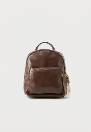 Väike pruun nahast seljakott esist lukuga tasku ja ümmarguse käepidemega, valge tausta ees eksponeeritud.