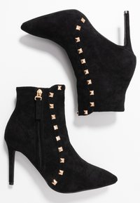 Bottines en daim noir avec bouts pointus, talons aiguilles et accents cloutés dorés le long du côté. Fermeture éclair latérale incluse.