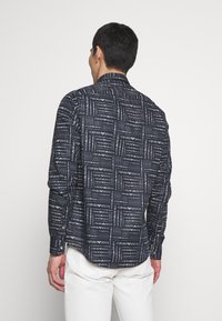 Camisa de manga larga en azul marino con un patrón geométrico de texto en contraste, que presenta un cuello puntiagudo y puños con botones, confeccionada en tela ligera.