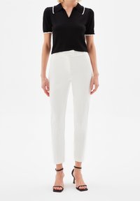Black short-sleeve polo top with white trim, paired with slim-fitting white trousers and block-heeled black sandals, showcasing minimalist design.