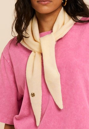 Donna che indossa orecchini a cerchio dorati, una morbida sciarpa color crema annodata al collo e una maglietta rosa a maniche corte con una piccola spilla dorata sulla sciarpa.