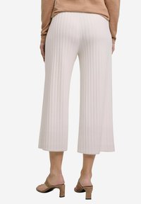 Jasno beżowe, prążkowane, krótkie spodnie o szerokim kroju, z teksturowanym wykończeniem i gładką talią, w zestawie z beżowymi sandałami na obcasie.