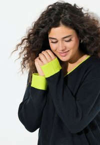 Svart tröja med långa ärmar, med ljusgröna ribbade mudd och halsringning. Mjuk textur med en avslappnad passform.