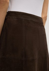 Bruine suède rok met een gladde textuur, voorzien van zichtbare stiksels en een hoge taille. De rits bevindt zich aan de linkerkant.