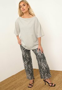 Blusa de gran tamaño en gris claro con mangas amplias, combinada con pantalones de pierna ancha en estampado de leopardo negro y gris, además de tacones negros con tiras. Fondo de textura tejida.