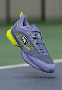 Violeta un neona dzeltena sporta apavi ar teksturētu augšdaļu, auklu dizainu un logotipu sānos. Viegls konstrukcija.