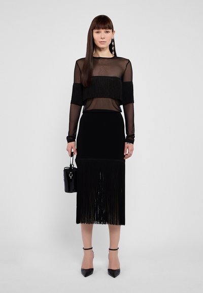 Sort fringing top med gennemsigtig materiale, parret med en tætsiddende sort nederdel med fringe detaljer. Tilbehør inkluderer en lille sort taske.