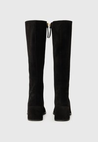 Bottes en suede noires jusqu'au genou avec un talon carré, dotées d'une fermeture éclair et de fins grelots en haut. Texture douce et design élégant.