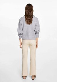 Gray knitted sweater with wide sleeves and ribbed hem paired with beige flared trousers. Rear view shows minimal detailing on clothing.