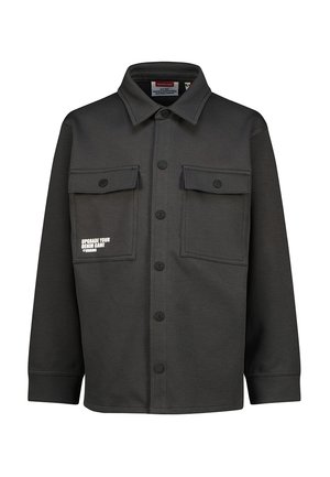 Black button-up shirt jacket with two chest pockets, one pocket featuring white text reading "Upgrade your denim game @Vingino."