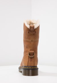 Bota de cuero marrón con un acabado texturizado, forro de piel sintética en la parte superior y un adorno de metal. Suela de goma plana con patrón.