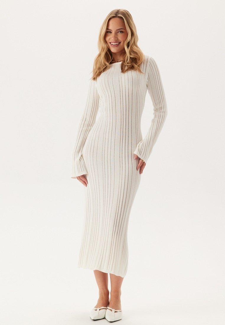 Abito a maniche lunghe in maglia a coste color avorio con una silhouette aderente, caratterizzato da maniche a campana e scollatura a barca. La texture è liscia e elastica.