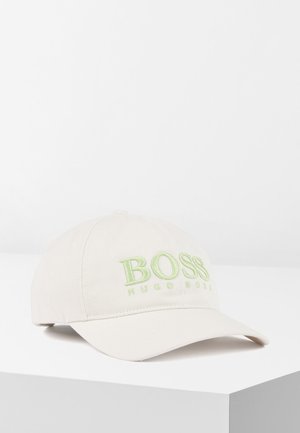 Beżowa czapka baseballowa z obciętym daszkiem, z jasnozielonym haftowanym logo "BOSS HUGO BOSS" z przodu, wyświetlana na białej powierzchni.