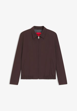 Bruine jas met ritssluiting en kraag, elastische zoom en zijzakken. Heeft een contrasterend rood binnenlabel. Gemaakt van een gladde stof.