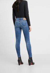 Jeans in denim blu slim con una finitura sbiadita, design a cinque tasche e una patch in pelle sul retro. Indossati con stivaletti neri con tacco.