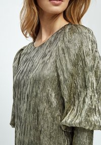 Metallisk guld topp med texturerad tyg, med en lös passform och puffärmar. Ytan har ett rutnätsmönster för ytterligare detalj.
